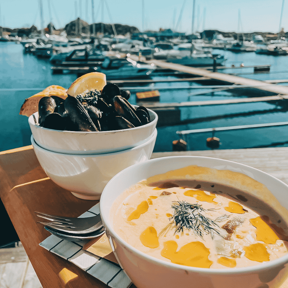 blåskjell og fiskesuppe på et bord med en båthavn i bakgrunnen