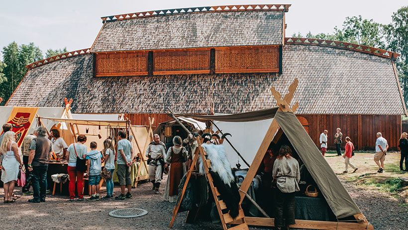 Teltleir foran en stor bygning med mennesker i historiske kostymer.