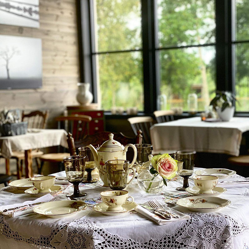 Elegant afternoon tea-oppdekking. Hvit duk med blondekant, tekanne, kopper og fat i porselen, og en rosa rose i vase