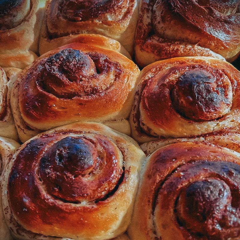 Nærbilde av en rekke nystekte kanelboller med gyllenbrun skorpe, stablet tett sammen.