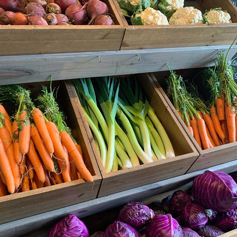 Vegetables in wooden boxes. Orange carrots, green leeks and purple cabbage in separate compartments. Fresh colours and clear organisation.