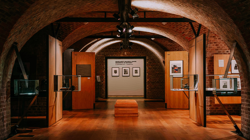 Utstillingsrom på Preus museum med murhvelvinger, trepaneler og glassmontere som viser fotografihistorie. Myk belysning skaper en stemningsfull atmosfære.