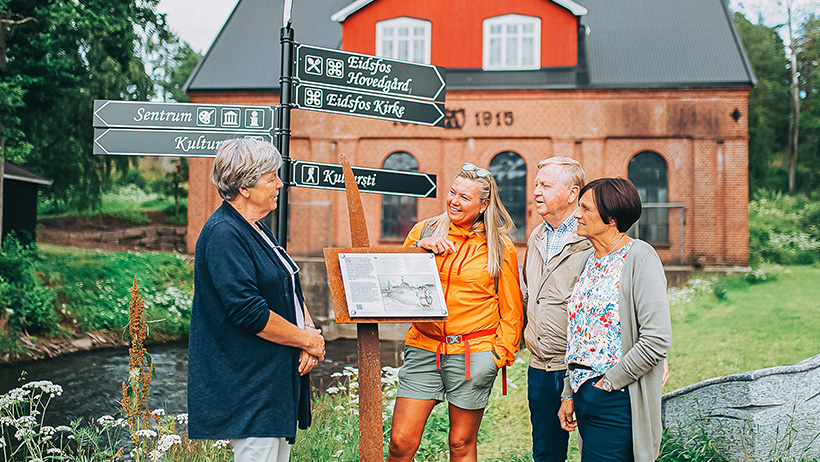 tre personer få guidet tur i Eidsfoss ved ett skilt