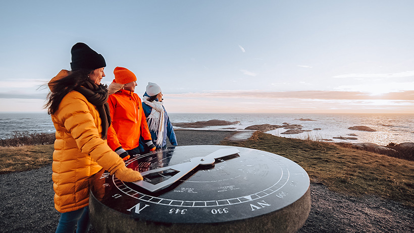 tre personer i turklær ved et solur rett ved havet