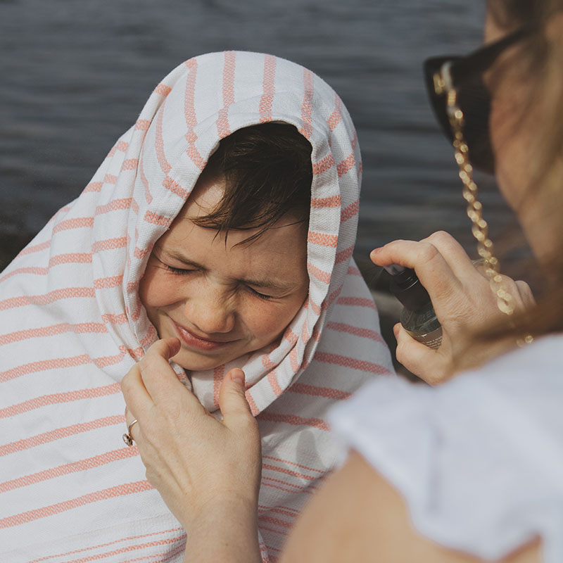 barn med håndkle rundt hode får solkrem smurt på seg av omsorgsperson