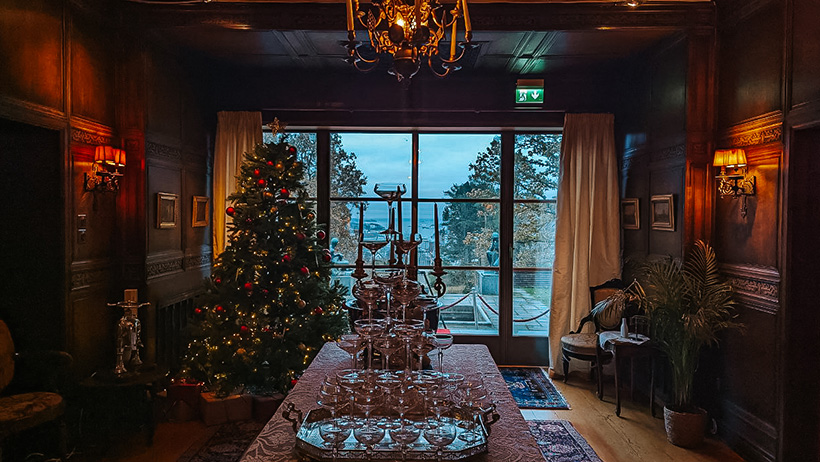 juletre i pyntet sal med champagneglasstårn på bord foran vindu