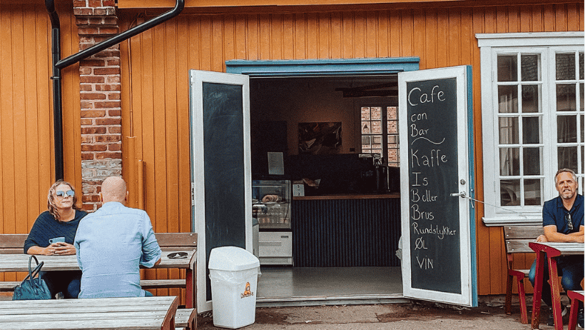 gult hus med meny på hver side av døren og benker med folk på hver side