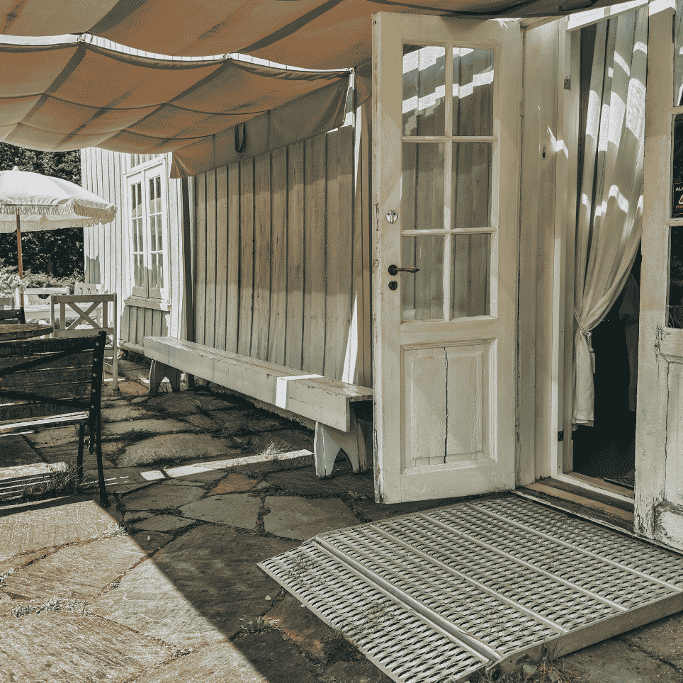 A metal ramp over a door threshold, with outdoor seating and a parasol in the background.