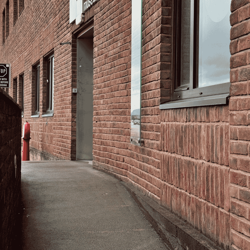A curved pavement running alongside a brick façade, with a red fire hydrant and a sign next to the footpath.