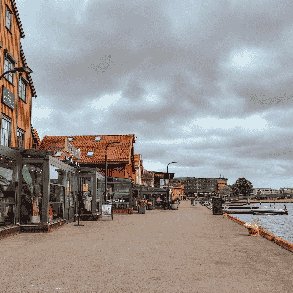 Trebrygge langs fargerike sjøhus, med glassfasader og uteservering ved vannet.