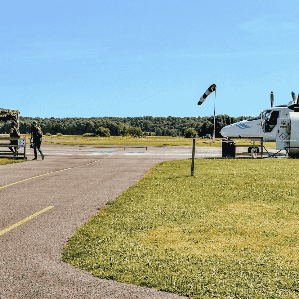 Rullebane med et lite fly, et vindpølseflagg og et overbygd venteområde.