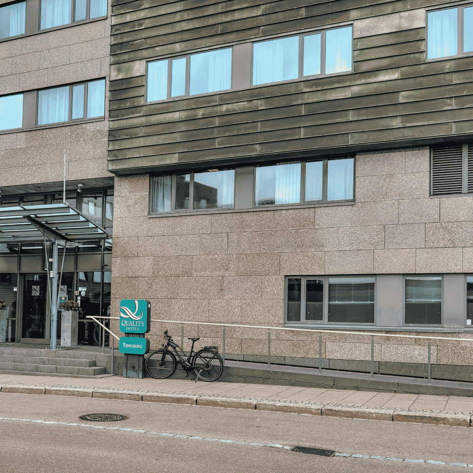 Hotellinngang med skilt og en sykkel parkert ved rekkverket utenfor.