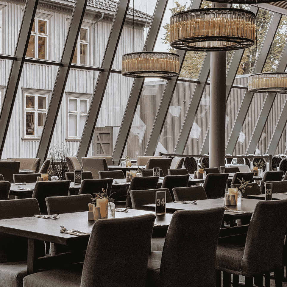 Restaurantlokale med skrått glasstak, hengelamper og nummererte bord.