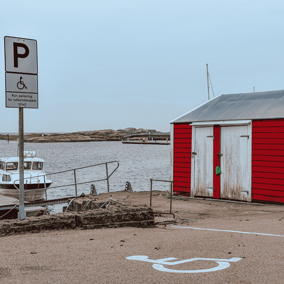 Rød bod med hvite dører og et HC-parkeringsskilt, med en båt fortøyd ved kaien.