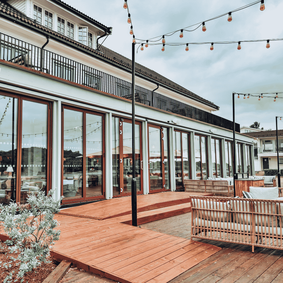Terrasse med glassdører, utependellamper og utemøbler i rotting utenfor en bygning.