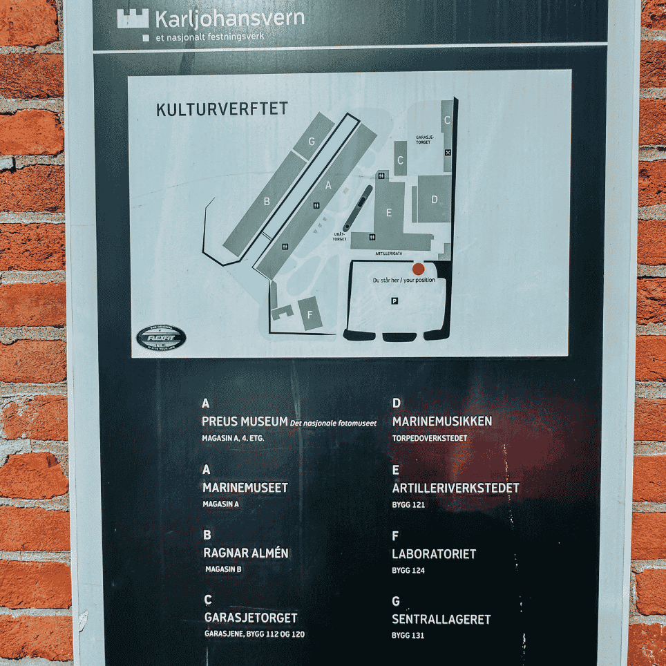An information board featuring a map of a museum site and a list of the buildings, attached to a brick wall