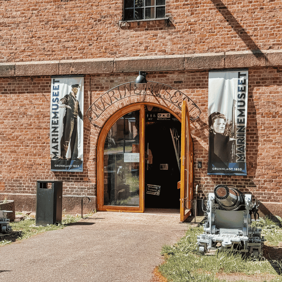 A brick building with a vaulted entrance, museum banners on either side and two old cannons positioned outside.