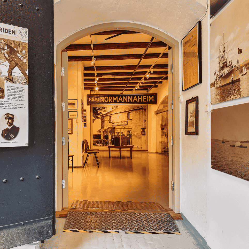 An exhibition room with a poster about a historical conflict, and a well-lit entrance to an adjoining room.