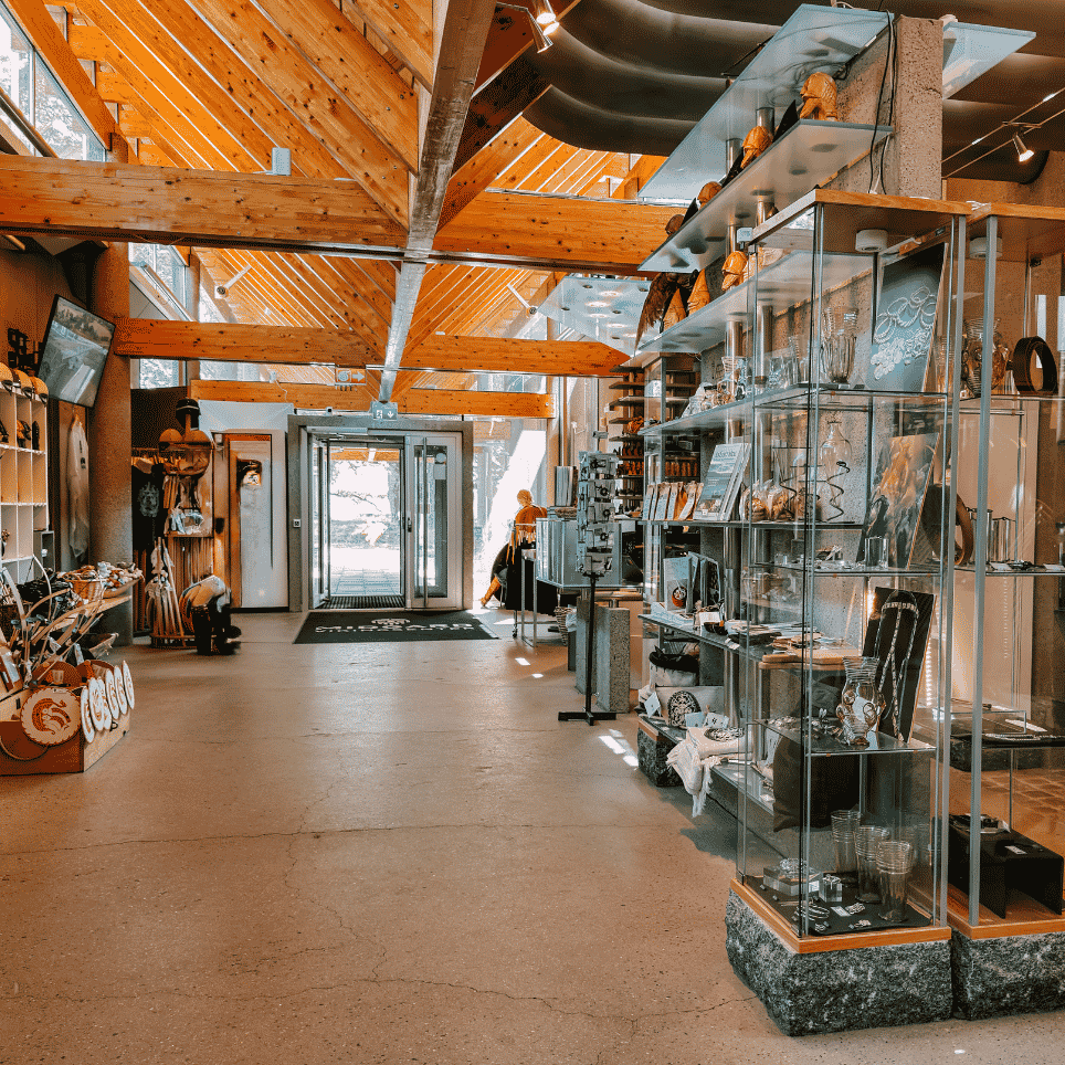 A museum shop with a sloping beamed ceiling, glass display cases containing jewellery and souvenirs, and shields on a display wall by the entrance.