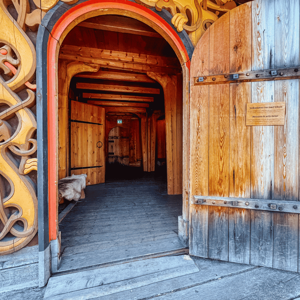 A carved portal with dragon motifs in yellow and red, featuring an open wooden door leading into a hallway.