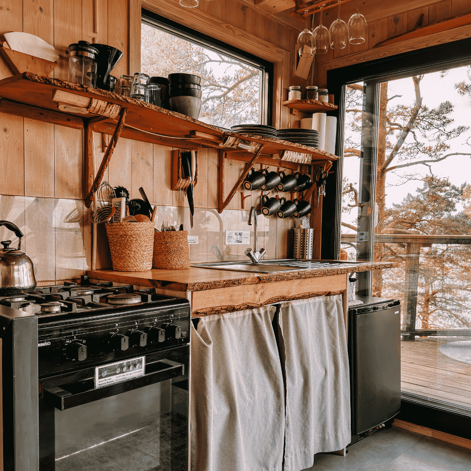 A wooden kitchen worktop with a gas hob, a sink and hanging cups, with a view through a window.