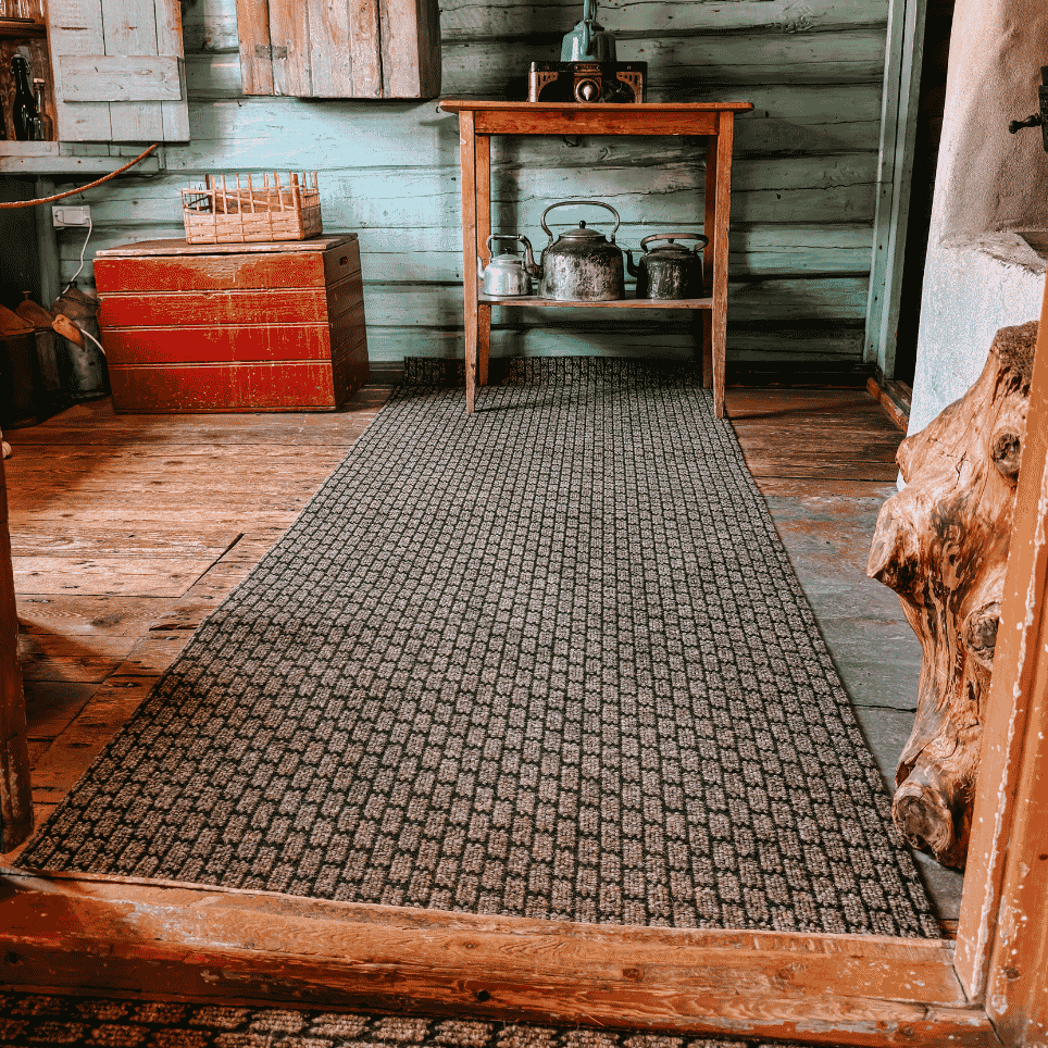 A green-painted kitchenette with a red wooden chest, pots hanging from a shelf and a woven rug on the floor.