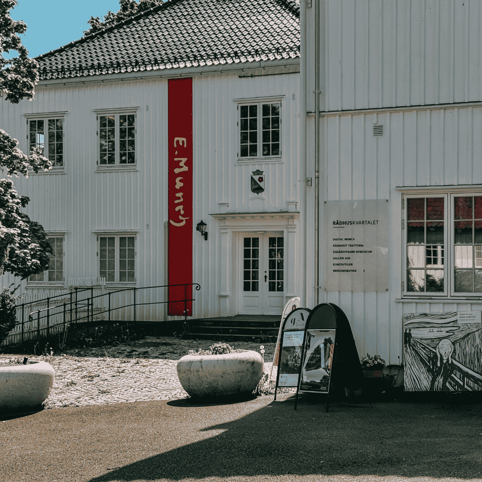 A white-painted building with a red vertical banner on the façade, next to a signpost outside the entrance.