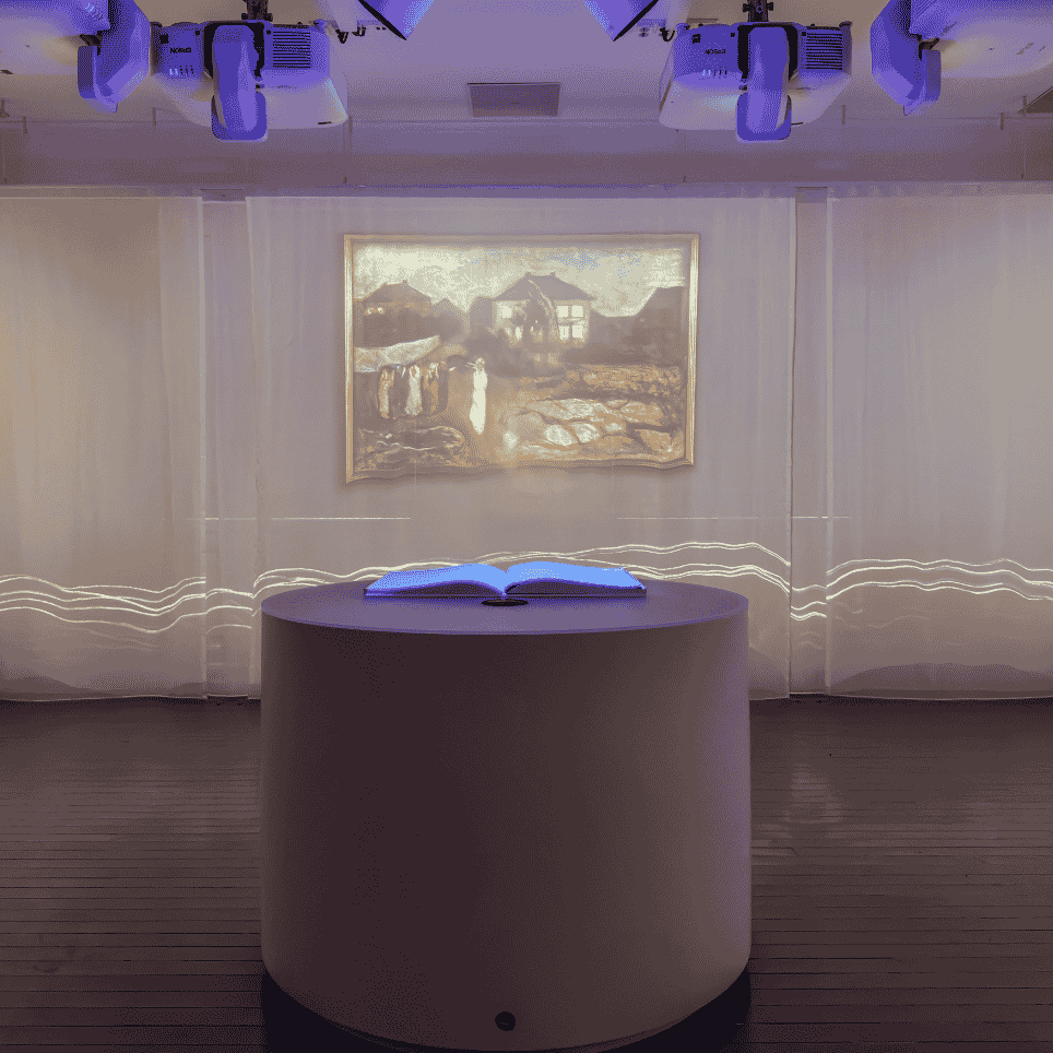 A dark exhibition space with paintings projected onto the walls, and an illuminated book on a round plinth in the centre.