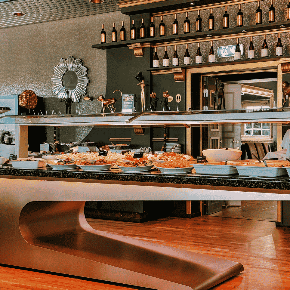 A restaurant with golden monkey sculptures and wine bottles on shelves, and salads displayed on a counter.