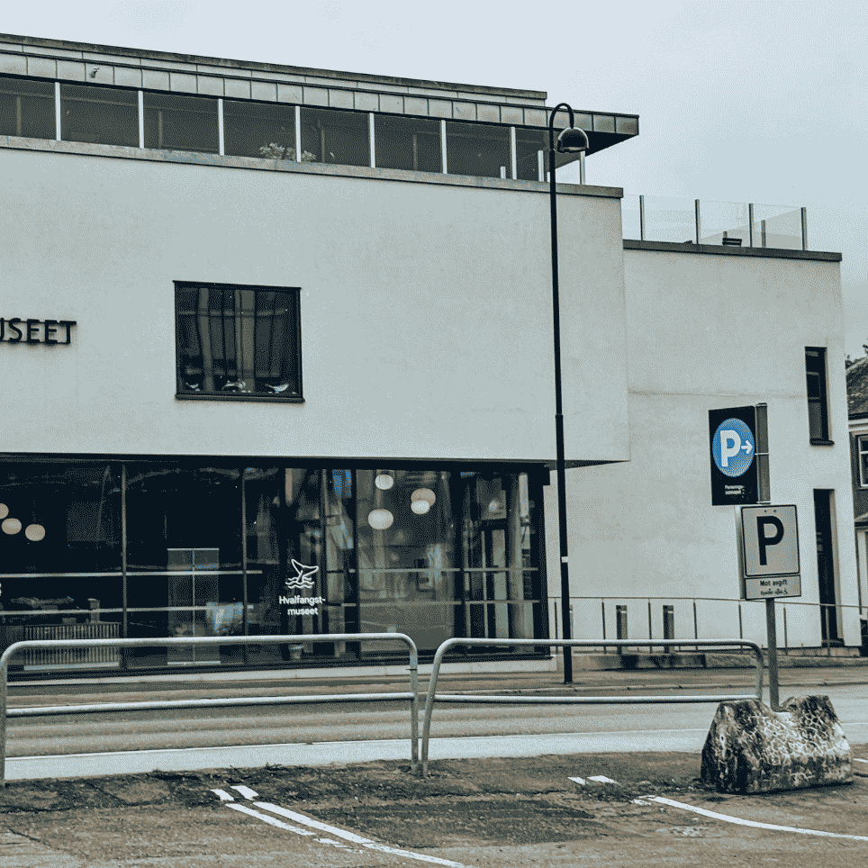 Fasaden til Hvalfangstmuseet, en hvit bygning med skiltet "HVALFANGSTMUSEET" og store vindusfelt mot gaten.