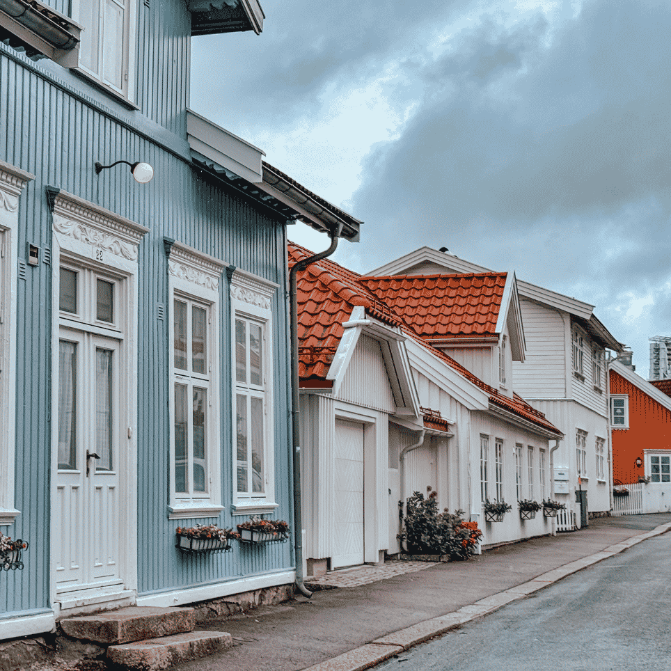 Lyseblått trehus med hvite vindusomramminger og blomsterkasser langs en norsk gate.