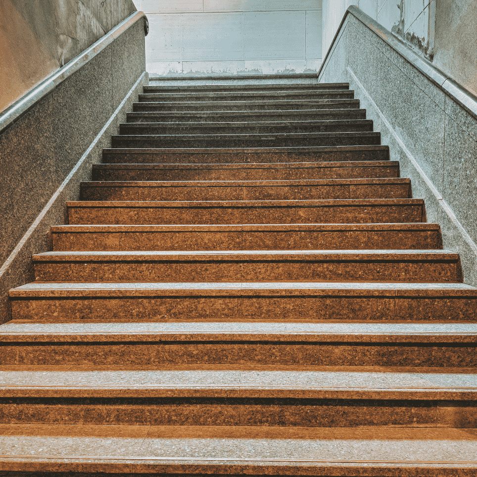 A wide stone staircase with a metal banister leading upwards to a bright concrete room.