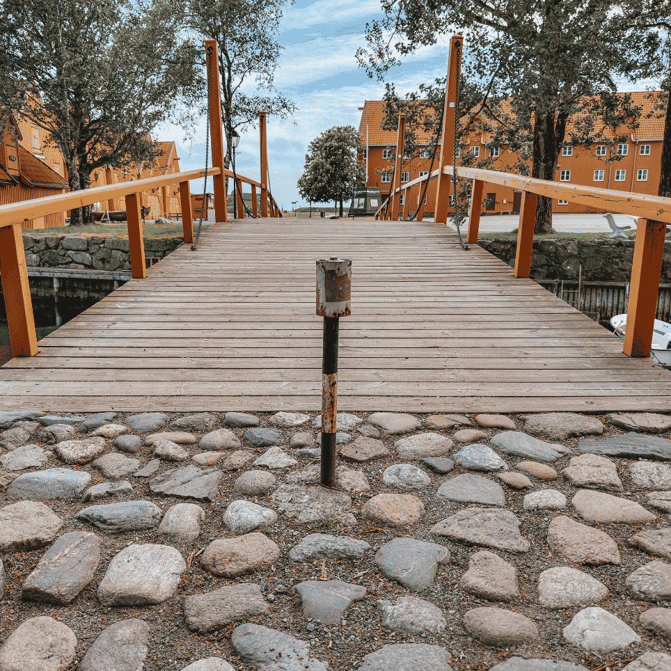 A wooden bridge with an orange railing spanning a canal, with rows of yellow timber buildings on either side.