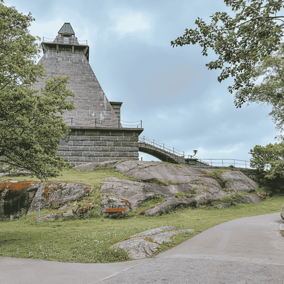 A pyramid-shaped stone monument seen from a distance through the treetops, with steps and a footbridge leading up to the top.