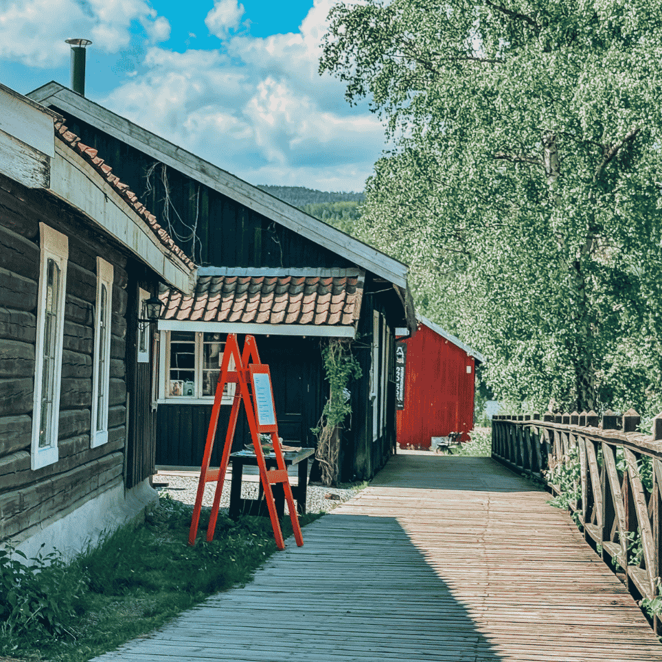 A wooden bridge and footpath between old wooden houses, with information signs and a bench