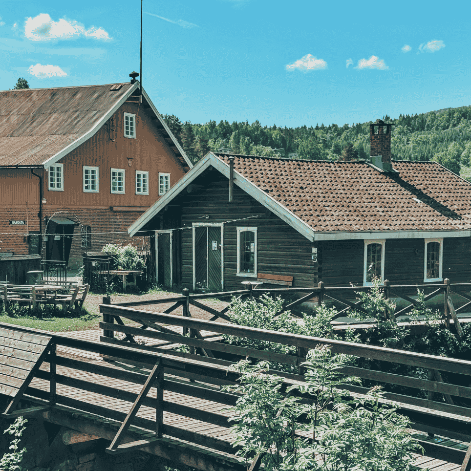 A street with dark and yellow wooden houses, seen from a wooden bridge.