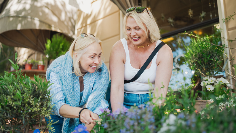 to personer holder blomster i hendene og står i en blomsterbusk