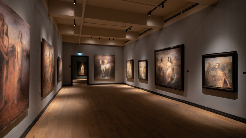 Interiør fra et kunstmuseum i Stavern med store malerier utstilt langs veggene i et stemningsfullt belyst gallerirom.